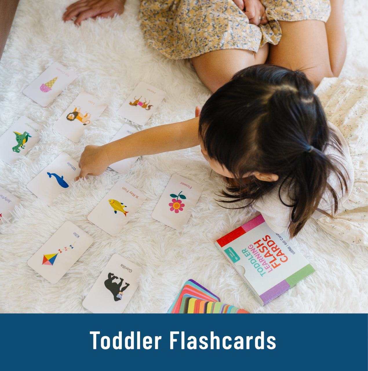 little girl laying on floor pointing to flash card with a blue whale on it on a white blanket