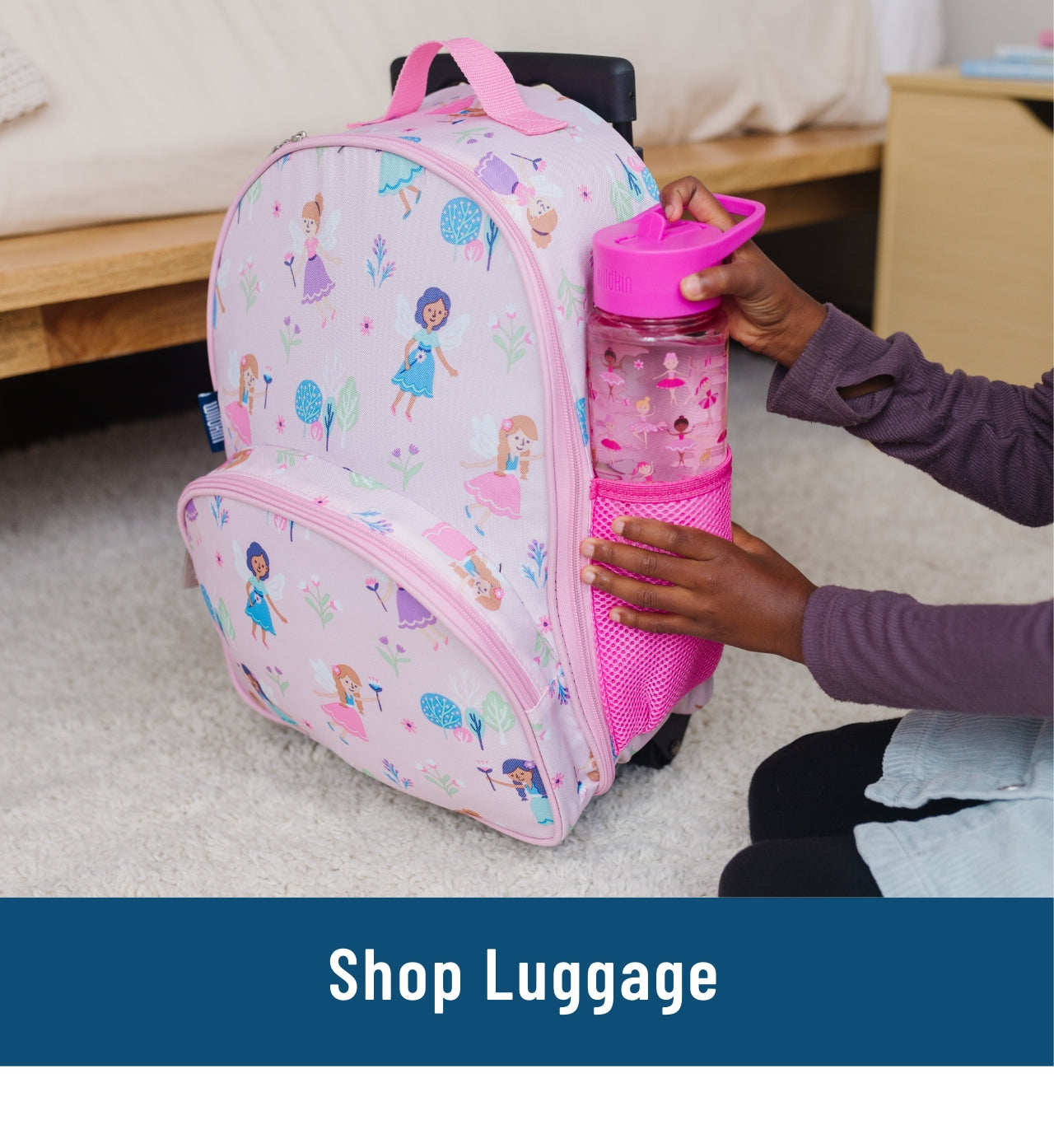 Image of a girl's hands putting a ballerina water bottle into the mesh side pocket of a rolling luggage suitcase with Fairy Garden pattern. Link to Shop Luggage